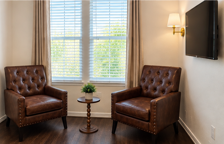 Two leather armchairs beside a window with a side table and a wall-mounted television
